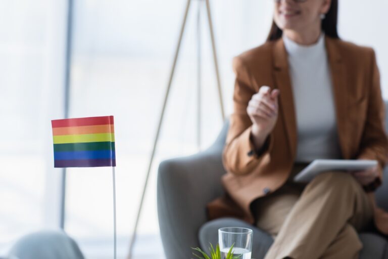 Small LGBTQ+ flag on the table in front of a female gender therapist