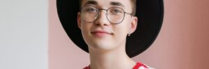 a young teenager wearing a hat, glasses, and a red striped shirt.
