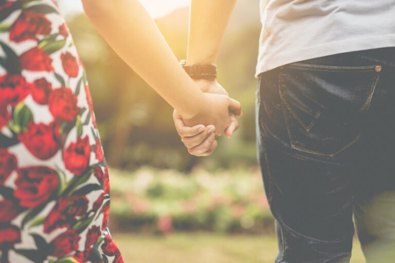 husband and wife holding hands as they walk toward a field of flowers